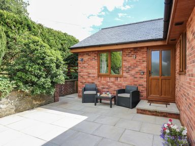 A patio area with two chairs and a table outside a brick house at Awel y Bryn in Rhayader