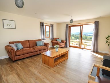 A living room with brown sofas coffee table and large glass doors with a view at Awel y Bryn in Rhayader