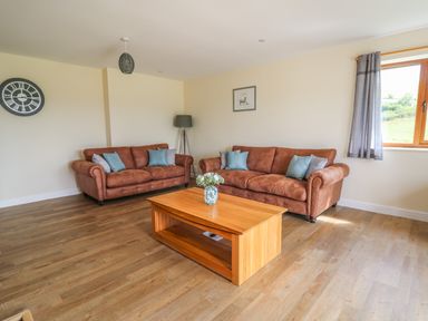 A living room with two brown sofas a wooden coffee table a floor lamp and a window with curtains at Awel y Bryn in Rhayader