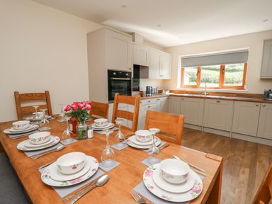 A kitchen with wooden dining table set for six people and beige cabinets at Awel y Bryn in Rhayader