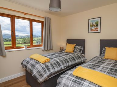 A bedroom with two single beds with plaid bedding and yellow throws near a window with a countryside view at Awel y Bryn in Rhayader