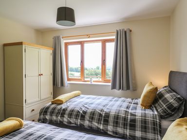 A bedroom with two single beds with plaid bedding gray curtains a wooden wardrobe and a window at Awel y Bryn in Rhayader