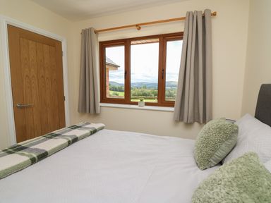A bedroom with a bed pillows a blanket a window with curtains and a wooden door at Awel y Bryn in Rhayader
