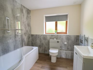 A bathroom with a bathtub shower combination a toilet a sink with a cabinet and a window with a roller blind at Awel y Bryn in Rhayader