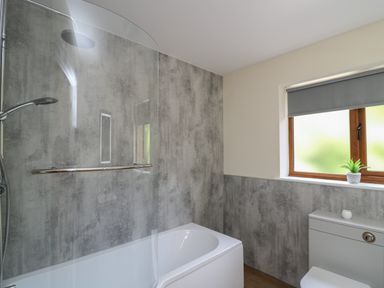 A bathroom with bathtub shower combo a frosted window and a toilet at Awel y Bryn in Rhayader