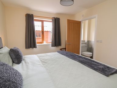 A bedroom with a double bed pillows and blanket next to window and an open door showing a bathroom at Awel y Bryn in Rhayader