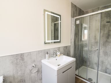 A bathroom with a sink vanity unit and illuminated mirror next to a glass shower enclosure at Awel y Bryn in Rhayader
