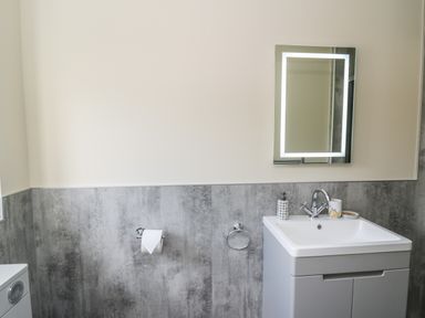 A bathroom with a sink, illuminated mirror, soap dispenser, and toilet paper at Awel y Bryn in Rhayader