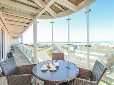 A balcony with a round glass table and four wicker chairs overlooking buildings and a road at Sunset View in Castletown Portland