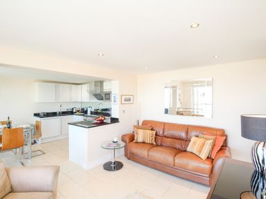 A living room with a brown leather sofa and a kitchen area with white cabinets at Sunset View in Castletown Portland