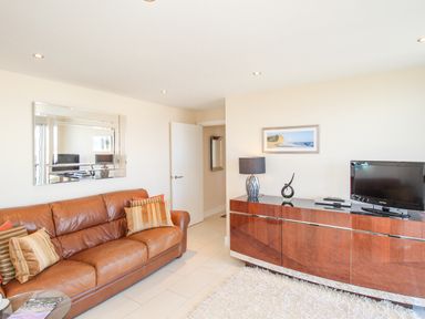 A living room with a brown leather sofa cushions a wall mirror a wooden cabinet with a TV lamp and decorative items at Sunset View in Castletown Portland