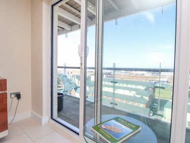 A glass door opening to a balcony with a view of buildings and a book on a round glass table at Sunset View in Castletown Portland