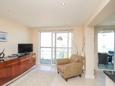 A living room with a beige armchair a wooden cabinet a television and sliding glass doors leading to a balcony at Sunset View in Castletown Portland