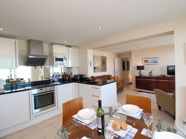 A kitchen and dining area with a glass table set for four and a living room with a TV and sofa at Sunset View in Castletown Portland