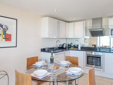 A kitchen with a glass dining table set with bowls and glasses and white cabinets and an oven at Sunset View in Castletown Portland