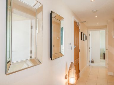 A hallway with two rectangular mirrors on the wall a wooden door three framed pictures a wicker floor lamp and a tiled floor at Sunset View in Castletown Portland