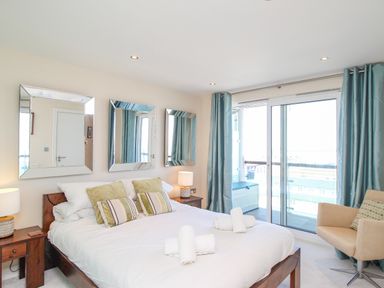 A bedroom with a bed and pillows bedside tables with lamps three mirrors on the wall a sliding glass door with curtains and a chair at Sunset View in Castletown Portland