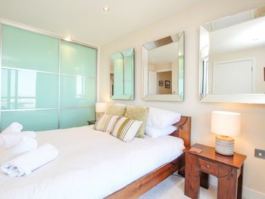 A bedroom with a wooden bed with white bedding and pillows and three wall mirrors above the bed at Sunset View in Castletown Portland