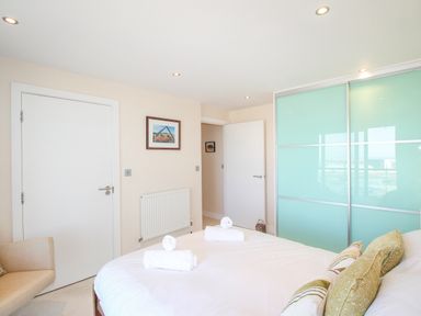 A bedroom with a bed with folded towels and cushions a beige armchair white doors and a large wardrobe with frosted glass doors at Sunset View in Castletown Portland
