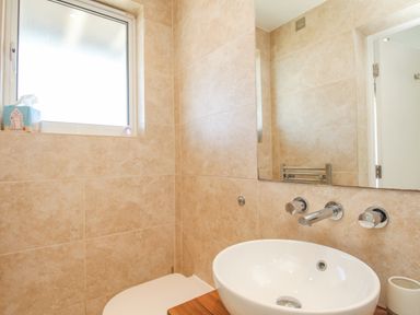 A bathroom with a round white sink a wall-mounted faucet a mirror a window and a tissue box on the windowsill at Sunset View in Castletown Portland