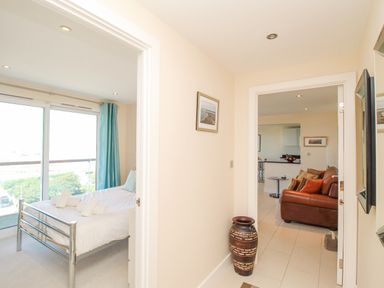 A hallway with a framed picture and a large vase leading to a bedroom with a bed and a living room with a brown sofa at Sunset View in Castletown Portland