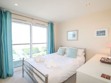 A bedroom with a metal bed frame white bedding rolled towels two blue pillows blue curtains a white dresser and framed pictures on the wall at Sunset View in Castletown Portland