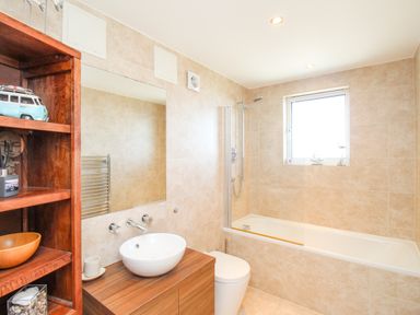 A bathroom with a bathtub shower combination a wooden vanity with a round white sink and a wooden shelf unit at Sunset View in Castletown Portland