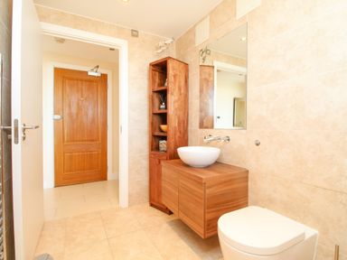 A bathroom with a wooden door a wooden cabinet and a round sink at Sunset View in Castletown Portland