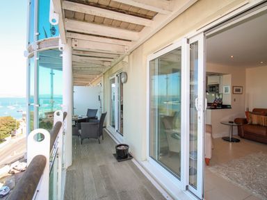 A balcony with wicker chairs and a table overlooking a body of water and a living room with a sofa and a rug at Sunset View in Castletown Portland