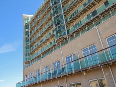 Exterior view of a multi-story building with glass balconies and a spiral staircase under a clear sky at Sunset View in Castletown Portland