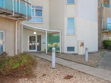 A building entrance with glass doors and a pathway surrounded by gravel and plants at Sunset View in Castletown Portland