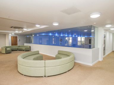 A seating area with curved green sofas and a glass wall showing an indoor pool at Sunset View in Castletown Portland