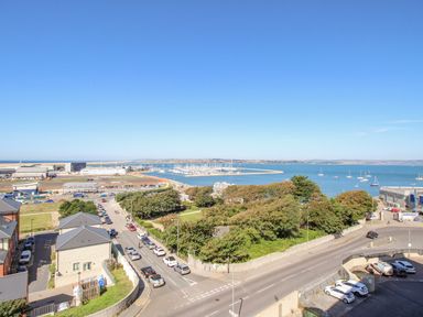 A view of a coastal town with roads cars trees a marina and boats on the water at Sunset View in Castletown Portland