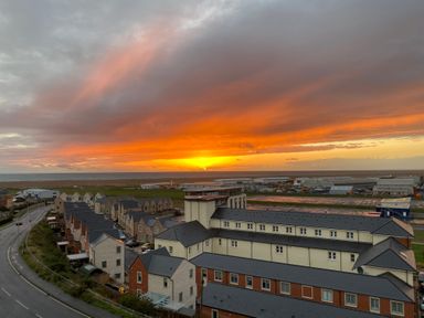 A residential area with rows of houses near a road and an industrial area with the sea and a sunset in the background at Sunset View in Castletown Portland