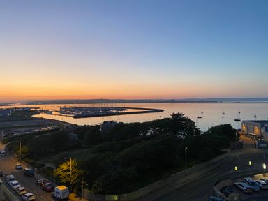 A harbor with boats and a shoreline at sunset with cars parked along the road at Sunset View in Castletown Portland