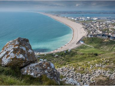 A coastal view with a rocky cliff overlooking a beach and a town with buildings and roads at Sunset View in Castletown Portland