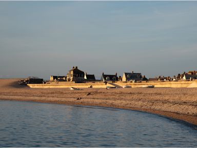 A pebble beach with boats and houses behind a sea wall at Sunset View in Castletown Portland