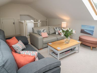 A sitting area with sofas a coffee table flowers and an ottoman at The Coach House in Bamburgh