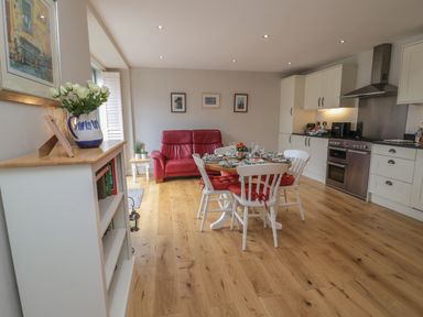 A kitchen dining area with a round table and white chairs with red cushions a red sofa and white cabinets with appliances at The Coach House in Bamburgh