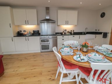 A kitchen with white cabinets a stainless steel stove and a dining table set with plates and glasses at The Coach House in Bamburgh