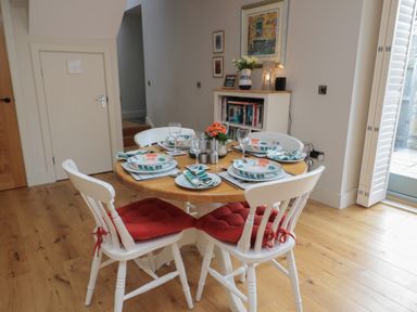 A dining room with a round wooden table set for four with white chairs with red cushions and plates with floral designs at The Coach House in Bamburgh