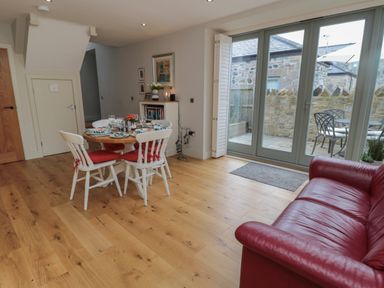 A dining area with a wooden table and four white chairs next to a red sofa and glass doors leading to a patio at The Coach House in Bamburgh