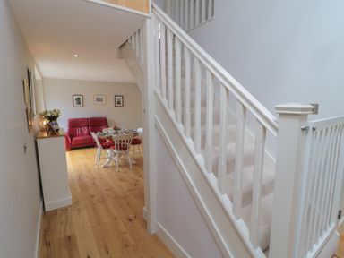 A hallway with wooden flooring leading to a dining area with a table and chairs and a red sofa at The Coach House in Bamburgh