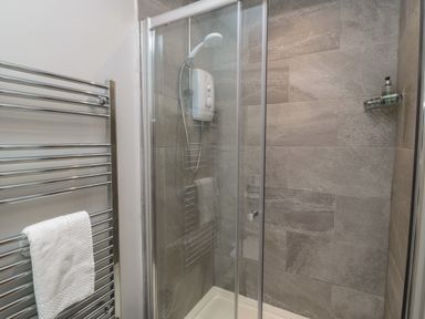 A shower with glass doors and a wall-mounted showerhead beside a towel rack with a white towel at The Coach House in Bamburgh
