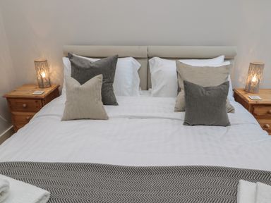 A bed with beige and gray pillows white sheets and wooden bedside tables with lamps at The Coach House in Bamburgh