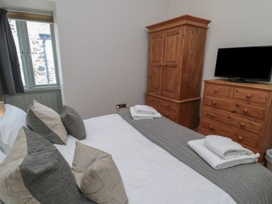 A bedroom with a bed cushions wooden wardrobe and chest of drawers with a TV at The Coach House in Bamburgh