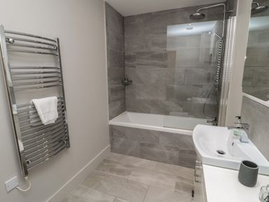 A bathroom with a bathtub shower combination and a towel rack at The Coach House in Bamburgh