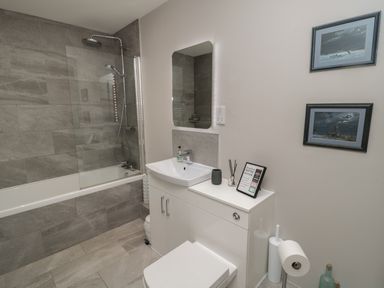 A bathroom with a bathtub and shower a sink with mirror and two framed pictures on the wall at The Coach House in Bamburgh