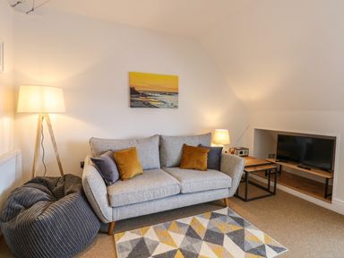 A living room with a grey sofa with pillows a patterned rug a bean bag floor lamp and a TV on a shelf at Flat 3 in Cromer