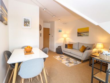 A living room with a dining table and chairs a sofa with cushions lamps and wall art at Flat 3 in Cromer